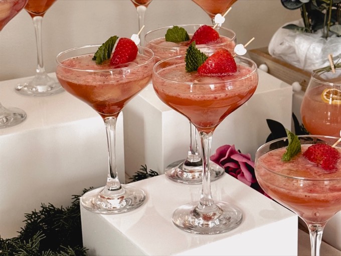 Elegant white-riser mocktail bar setup with florals and pink drinks
